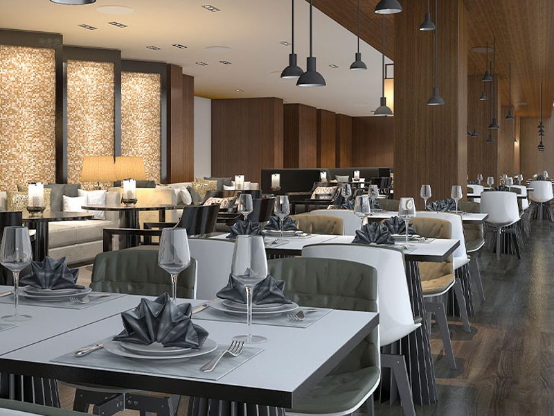 Elegant restaurant dining room with white tables, folded dark napkins, wine glasses, and cushioned chairs under pendant lights.