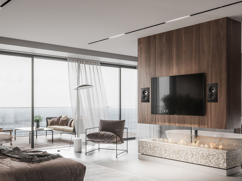 Modern living room with floor-to-ceiling windows overlooking the ocean, a wood-paneled wall with a mounted TV and built-in fireplace below.