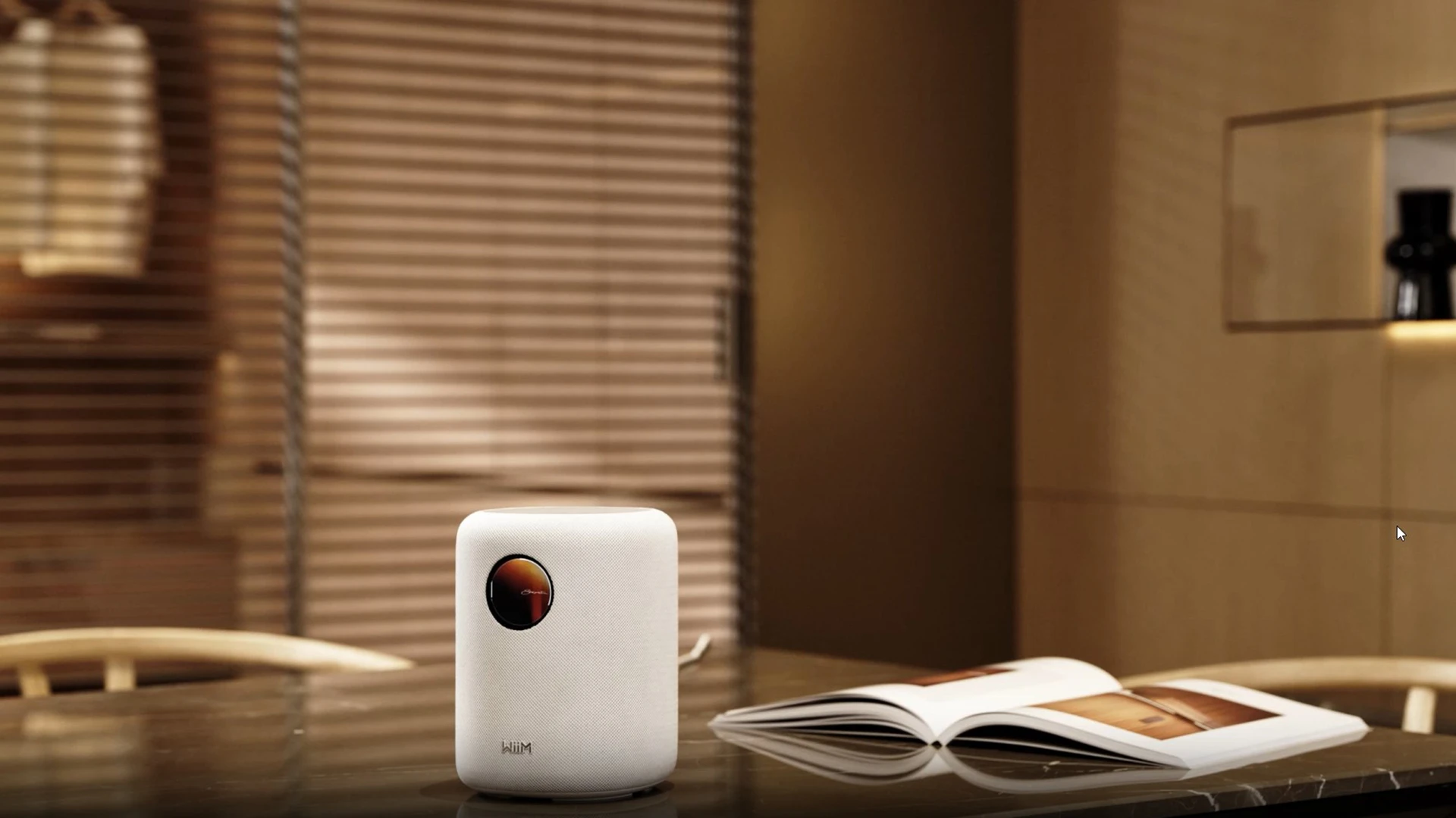 White compact speaker with a circular orange logo sits on a glossy table next to an open magazine in a modern interior backdrop.