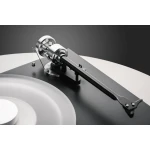 Close-up of a silver tonearm and cartridge on a turntable with a white vinyl record nearby for an informative view of a record player component.