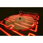 Circular platform outlined by glowing red LED strips forming a geometric pattern on a reflective surface, with a small mounting device on top.
