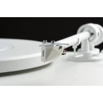 Close-up of a white turntable tonearm with an Ortofon cartridge and stylus over a white platter against a dark background.