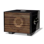 Black rectangular speaker with horizontal wooden slats front grille and visible round driver behind; glossy black exterior with small feet underneath