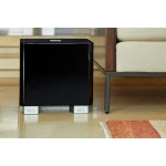 Compact, glossy black subwoofer on the floor under a beige sofa in a living room.