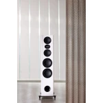Tall white floor-standing speaker with multiple circular drivers in a minimalist room beside a textured curtain on the right.