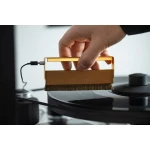 Person using a wooden brush to clean a vinyl record on a turntable.