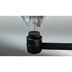 Close-up of a metal printer nozzle depositing material onto a textured black wheel at the end of a horizontal arm.