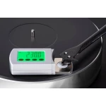 Close-up of a turntable with a digital scale showing 2.300 g on a green display, and a carbon-fiber tonearm resting over a vinyl record surface.