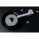 Close-up of a black vinyl record with a brushed metal tonearm on a dark surface.