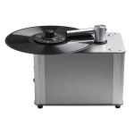 Turntable with a black vinyl record spinning on a metallic silver base, shown from a side angle.